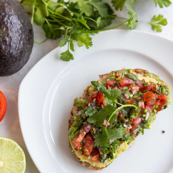 Pico de Gallo Avocado Toast on white plate with cilantro, avocado, tomato and lime around