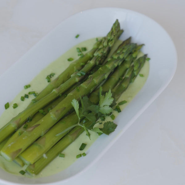 Asparagus presented with fresh cut herbs on a bed of avocado sauce