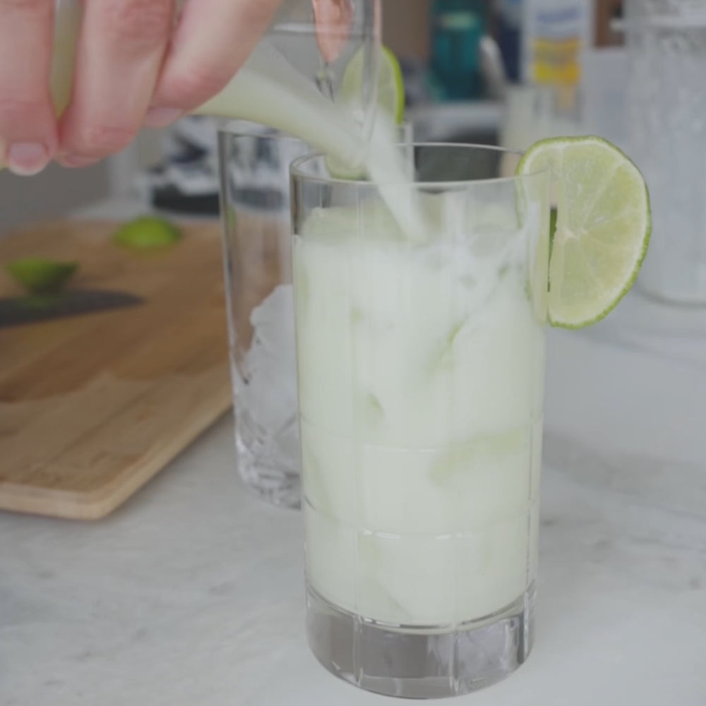 Fresh Lime Drink - Pouring Brazilian Limeade into a tall glasse with ice and a lime slice on the rim