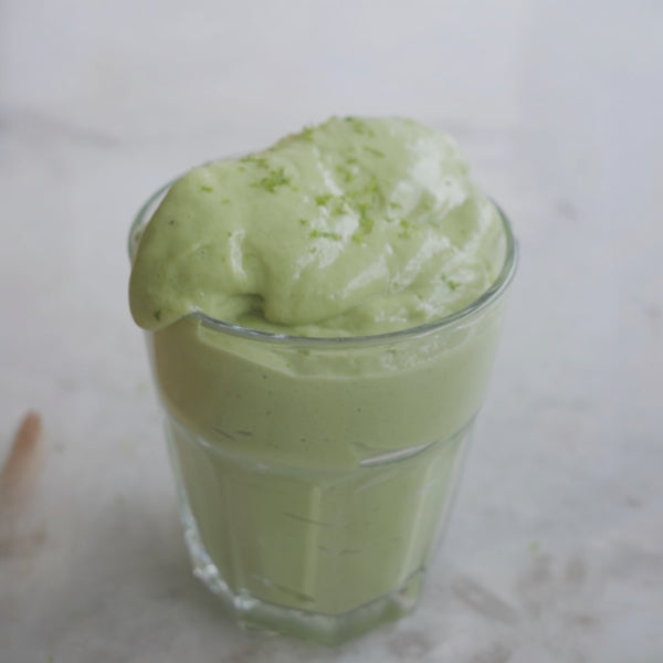 Avocado Smoothie poured in a clear glass with lime zest on top.