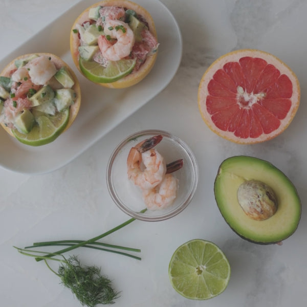 Shrimp, grapefruit and avocado salad presented in grapefruit halves on a serving plate with each ingredient placed next to it on our a counter