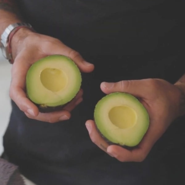 Ripe avocado halves held in open hands