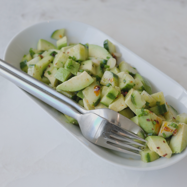 Avocado cucumber salad plated in a sharing dish with serving utensils