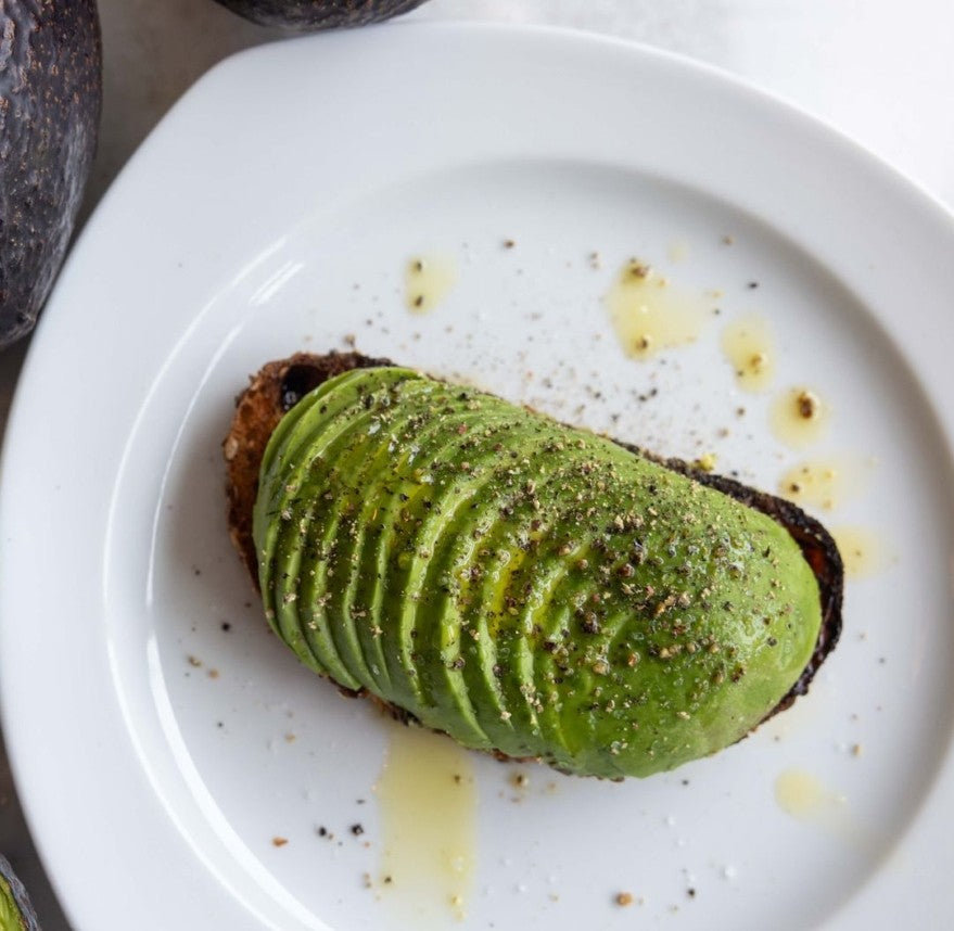 a piece of toast topped with sliced avocado, sprinkled with seasoning on a white plate