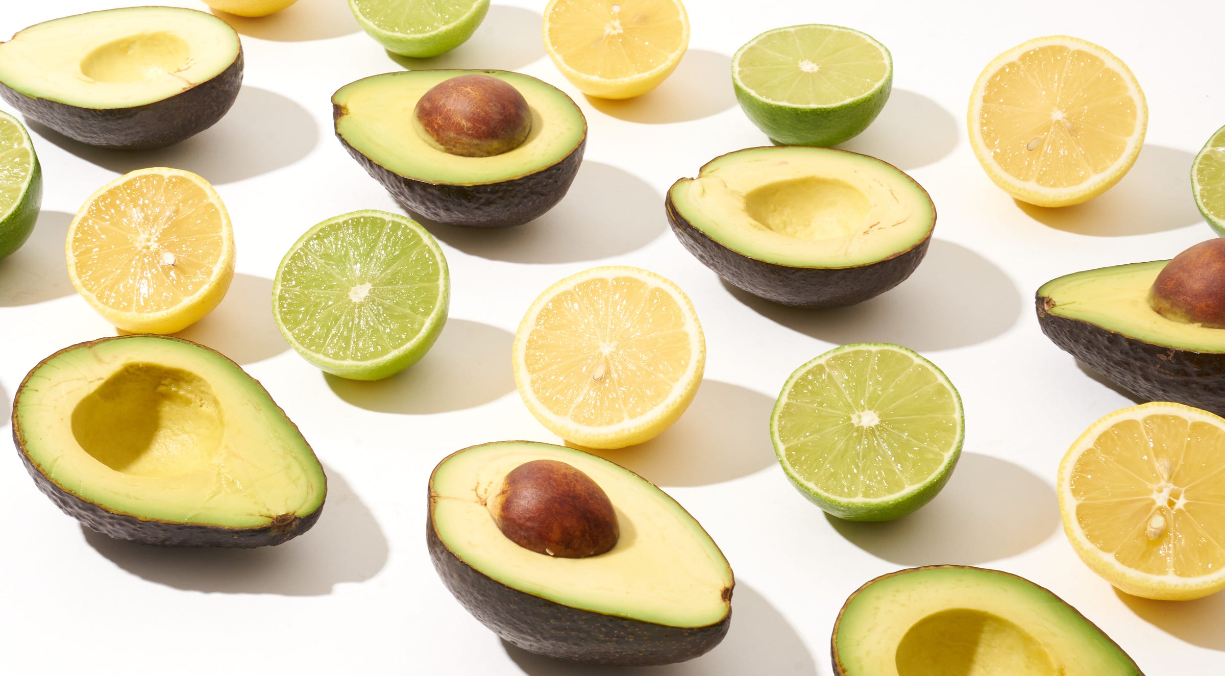 Fresh Avocados, limes and lemons cut open and line up in 4 rows on a white background