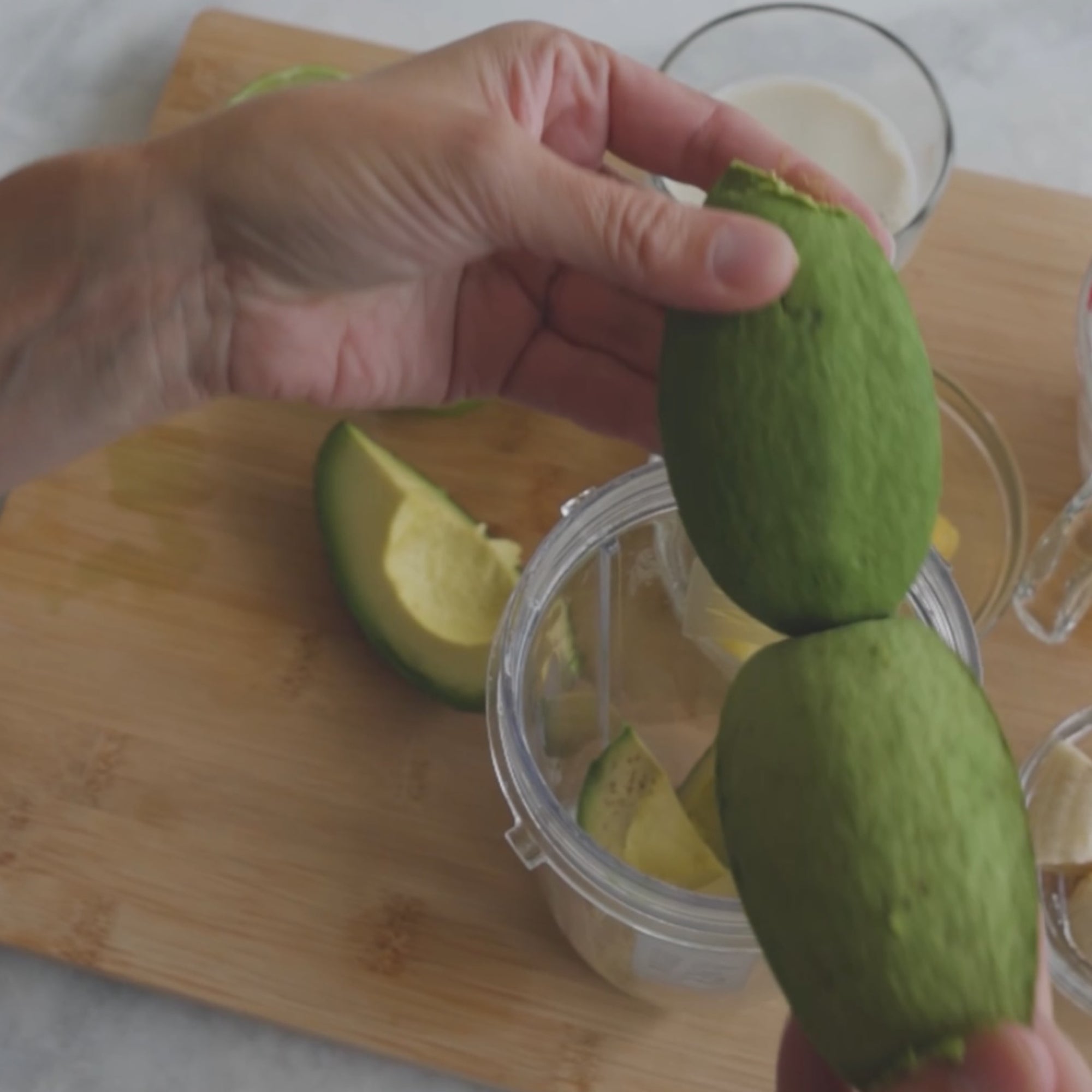 a person holding two limes, preparing to add them to a blender, with lime halves and other ingredients visible in the background