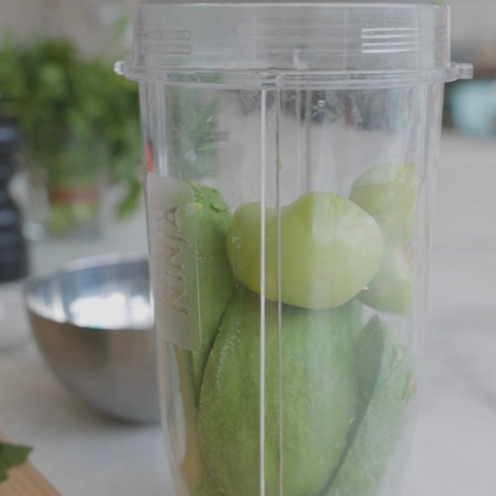 green tomatoes and other vegetables in a blender container