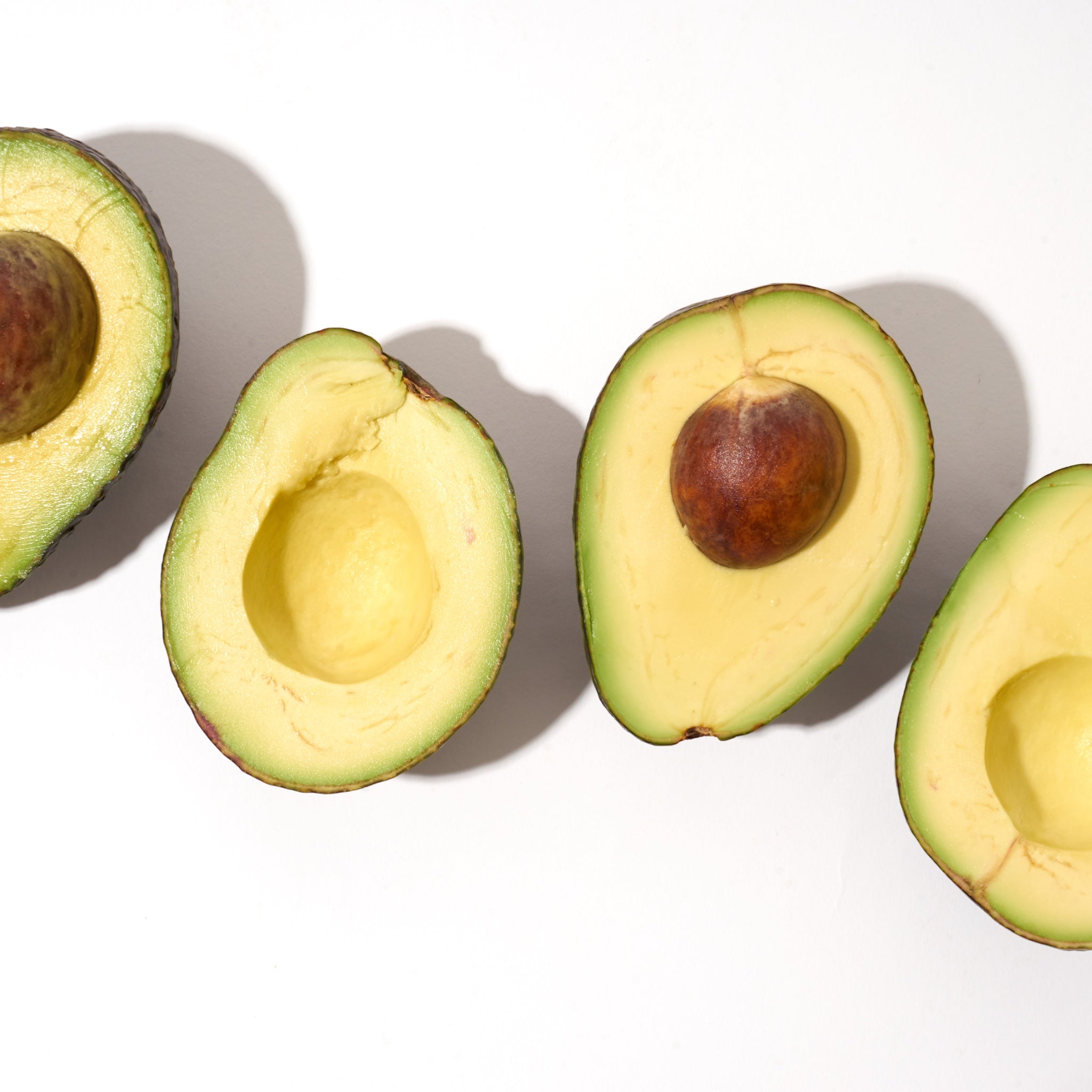 Fresh Avocados cut open and lined up on a white background