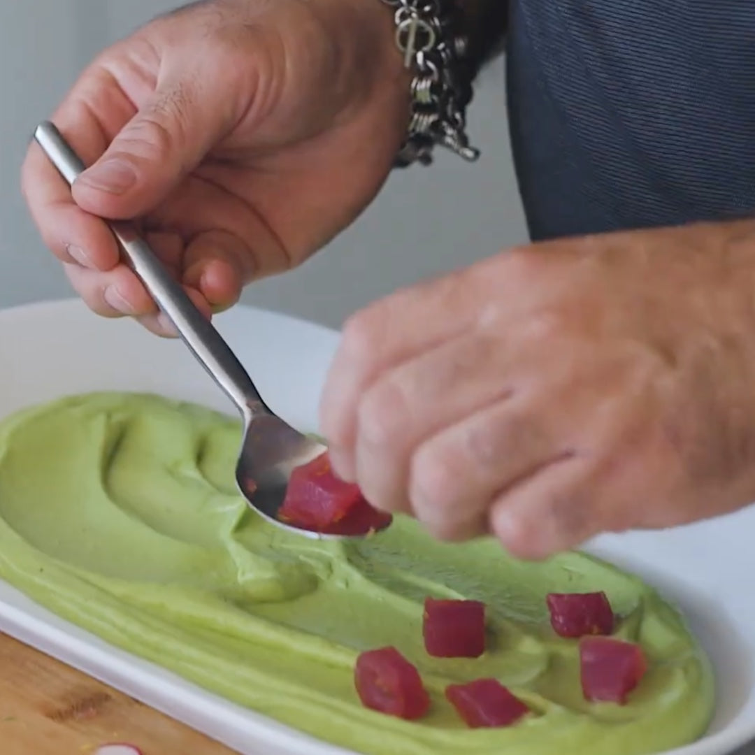 arranging diced tuna on a plate with a layer of creamy avocado puree using a spoon