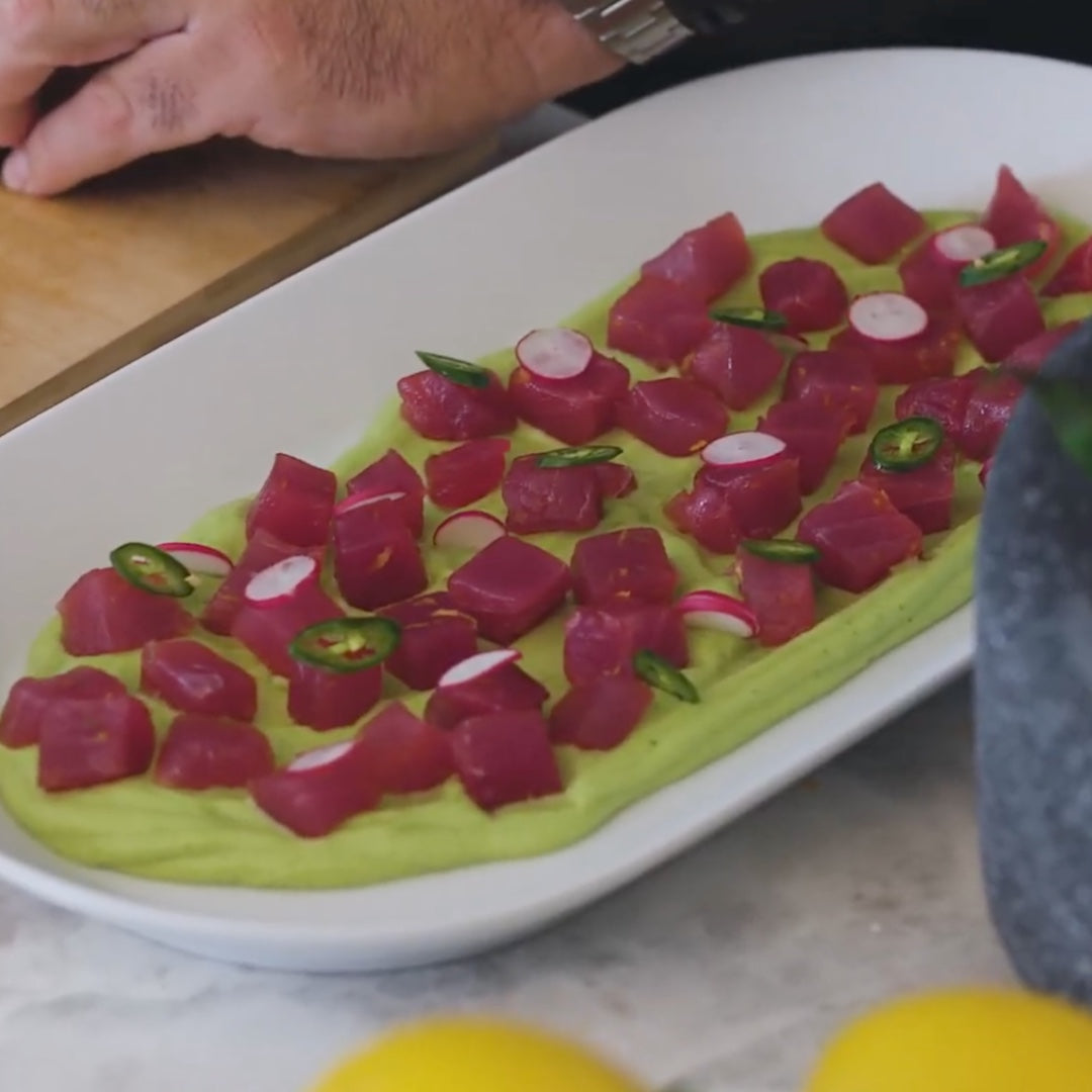 plated dish with diced tuna on a bed of avocado puree, garnished with sliced jalapenos and radishes