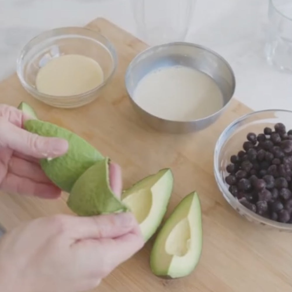 preparing avocados slices with bowls of blueberries and creamy ingredients on a cutting board