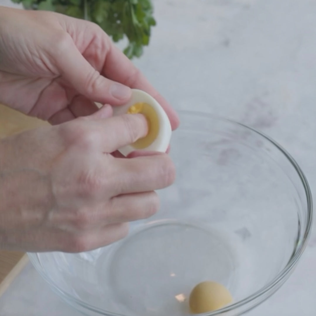 removing the yolk from a hard-boiled egg over a bowl