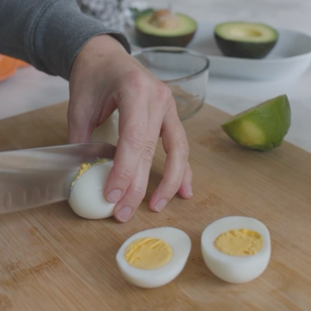 slicing a hard-boiled egg in half, with avocados in the background