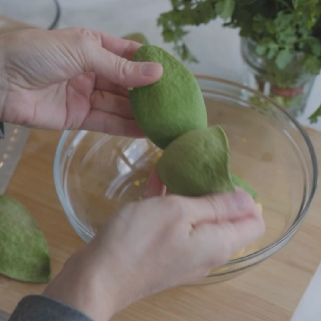 peeling an avocado over a bowl, with cilantro in the background