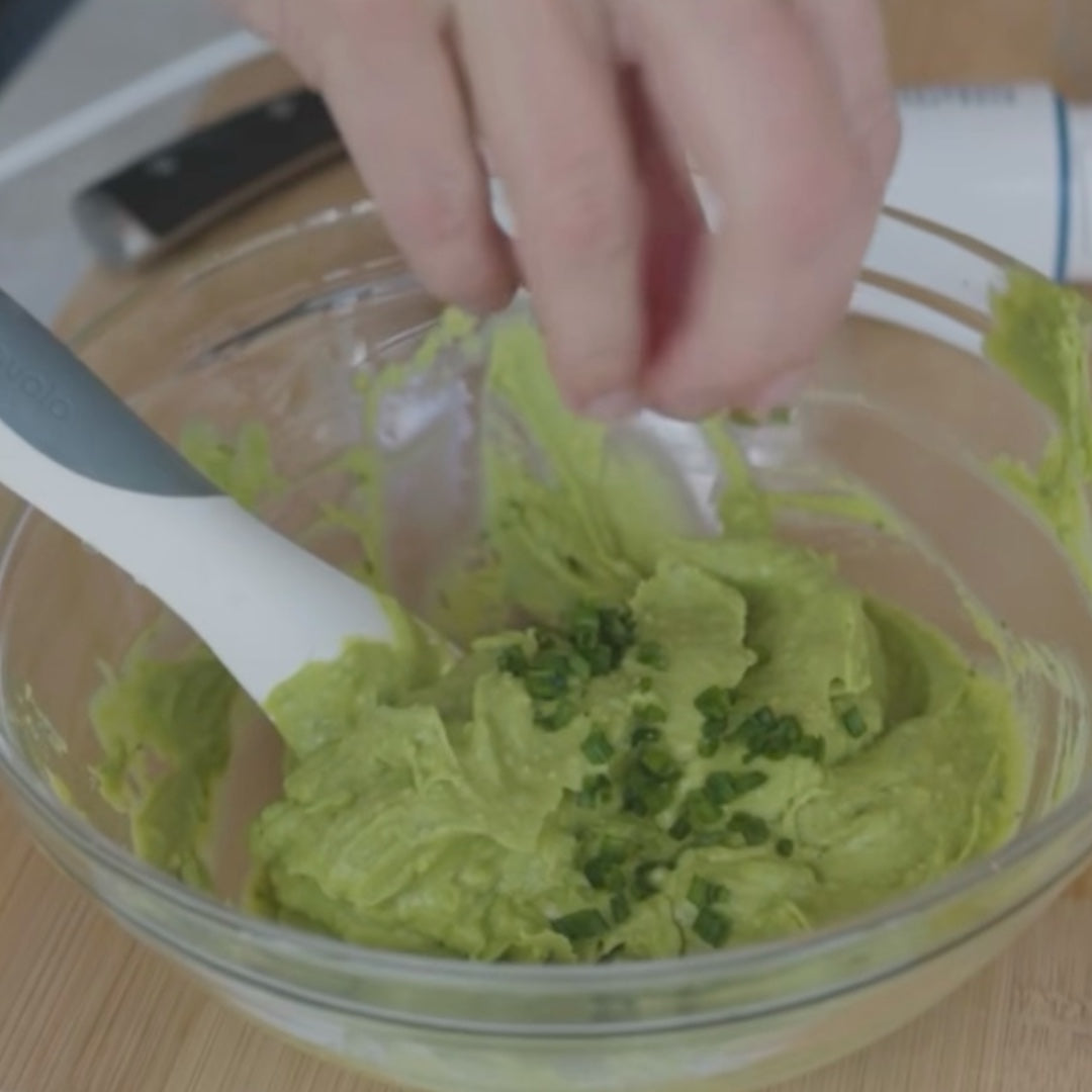 mixing avocado mash with chopped herbs in a bowl
