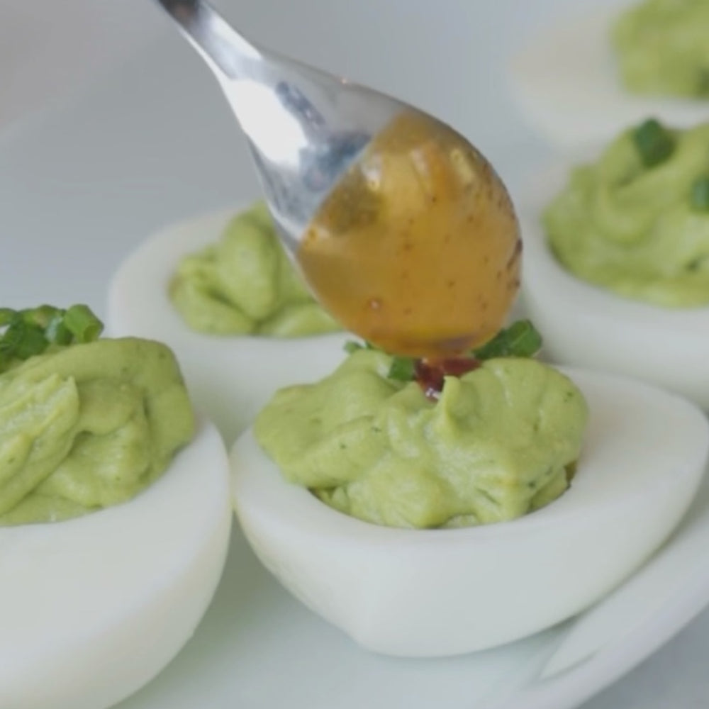 adding sauce to avocado-filled egg halves