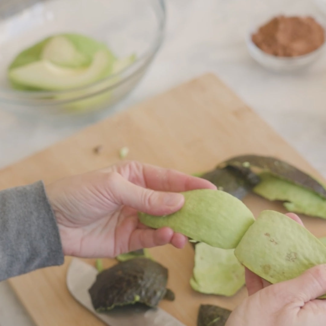 holding peeled avocado halves, with a bowl and spices nearby