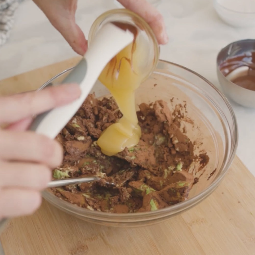 adding a mixture into a bowl with cocoa powder and other ingredients