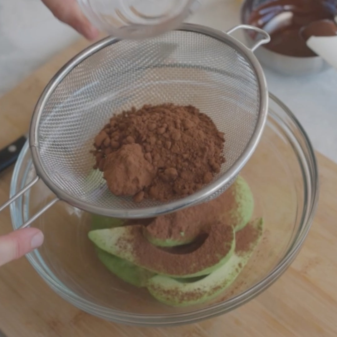 sifting cocoa powder over sliced avocados in a bowl