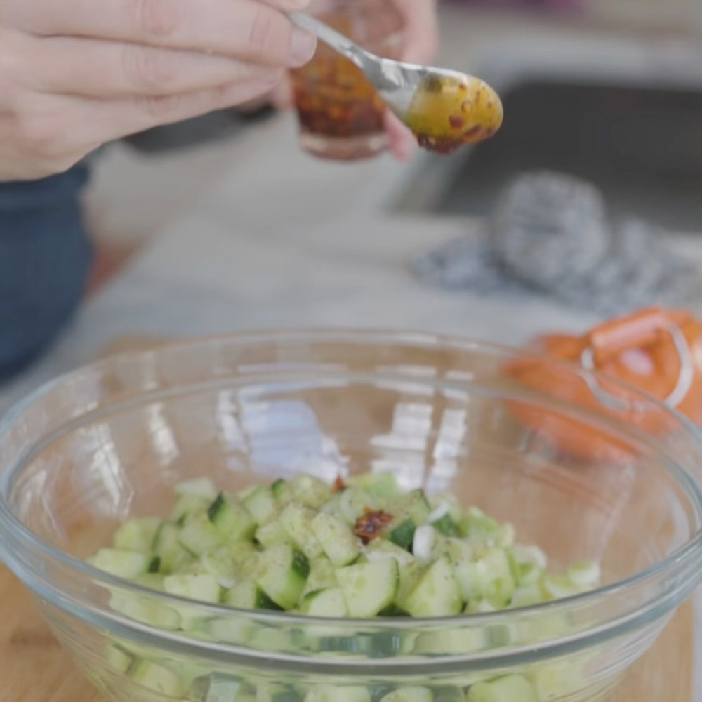 adding a spoonful of dressing to a baw of diced vegetables