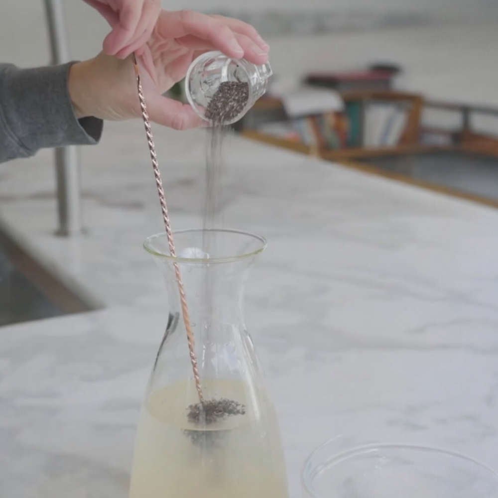 pouring chia seeds into a glass container with a spiral stirrer