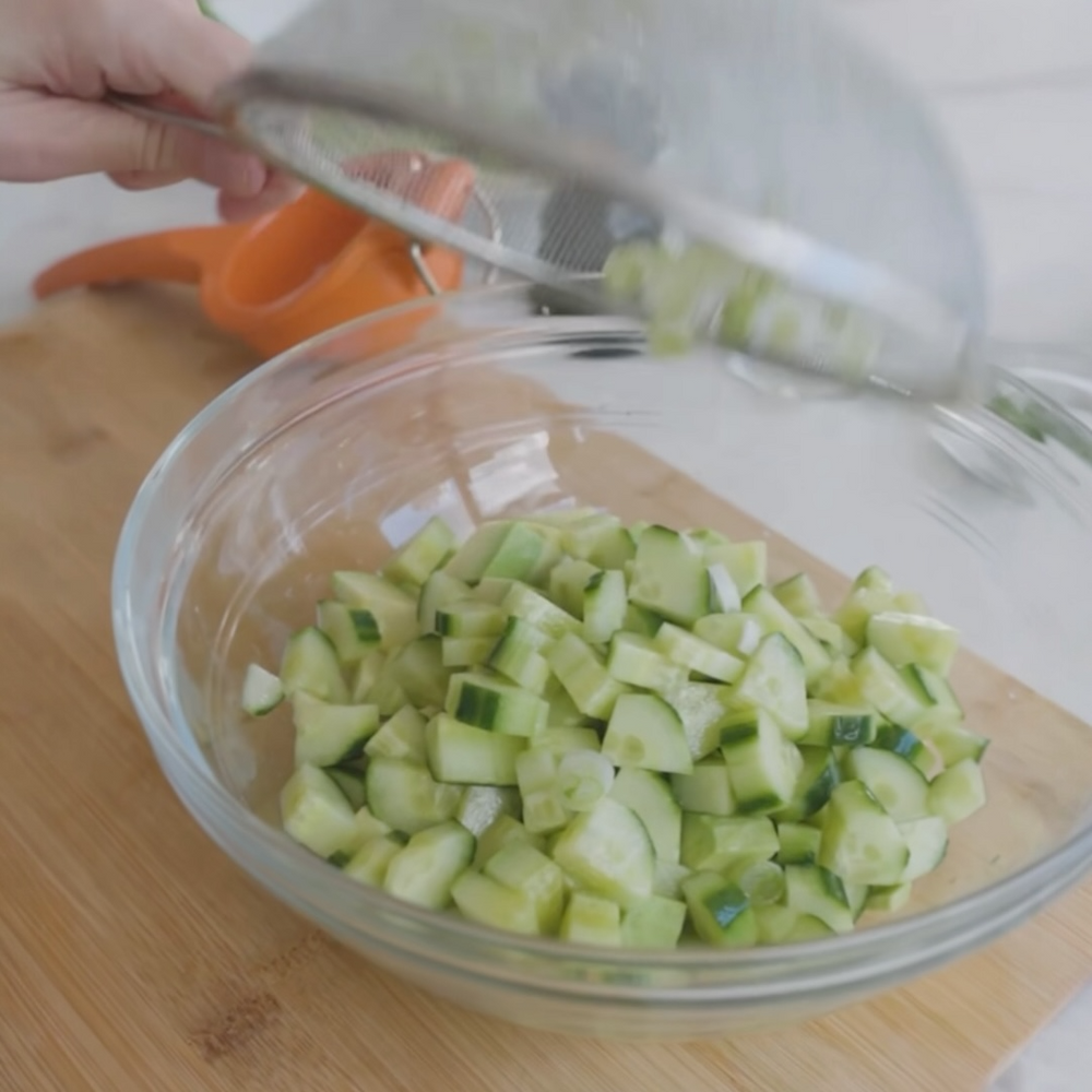 diced cucumber being placed into a glass bowl a spoon