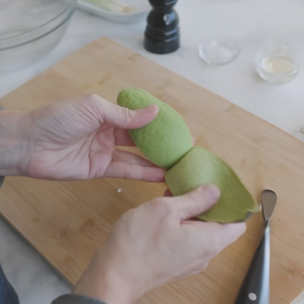 a person peeling an avocado on a wooden cutting board, with kitchen items nearby