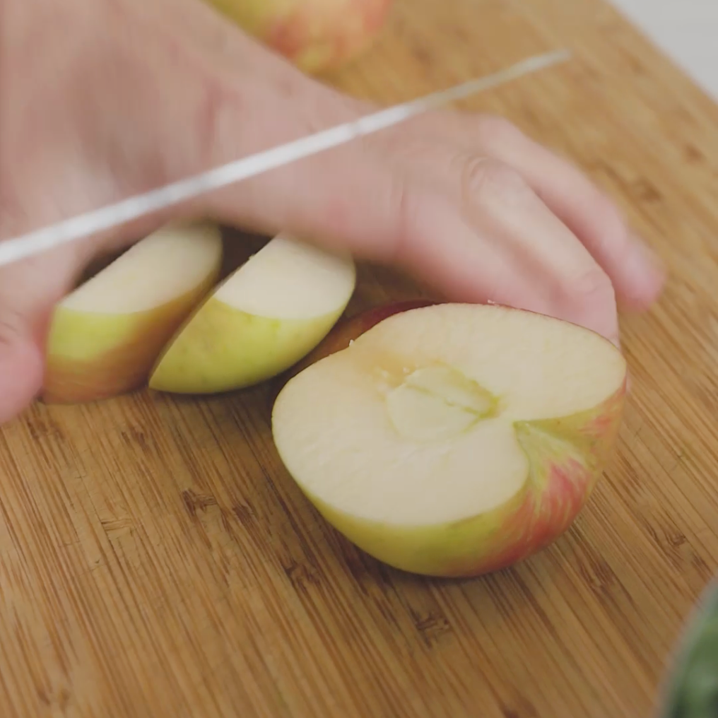 a person slicing an apple on a wooden cutting board