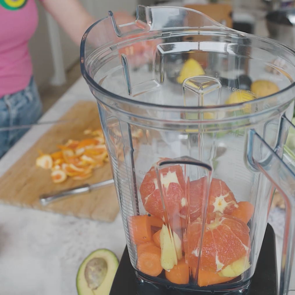 a blender filed with ingredients like grapefruit slices and carrots, ready for blending