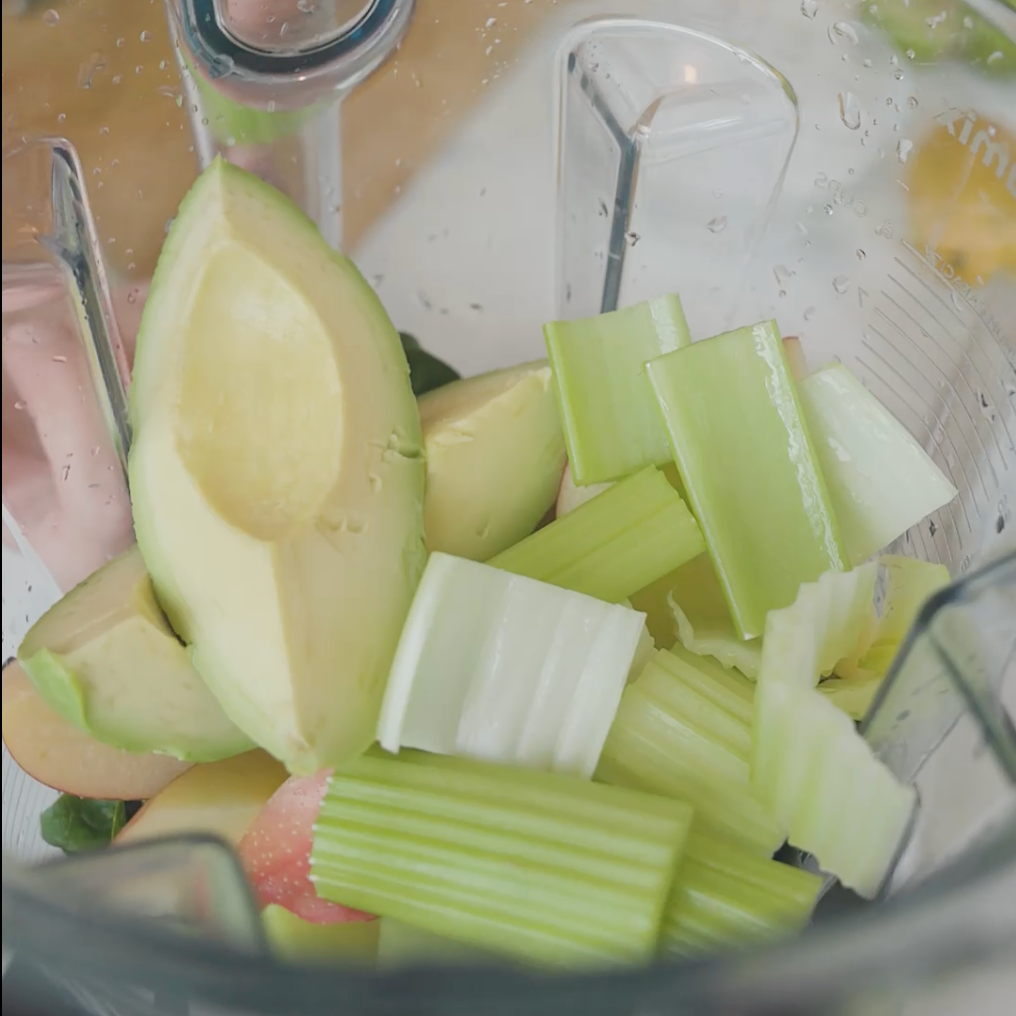 a blender filled with ingredients like avocado, celery pieces, and apple slices ready for blending.