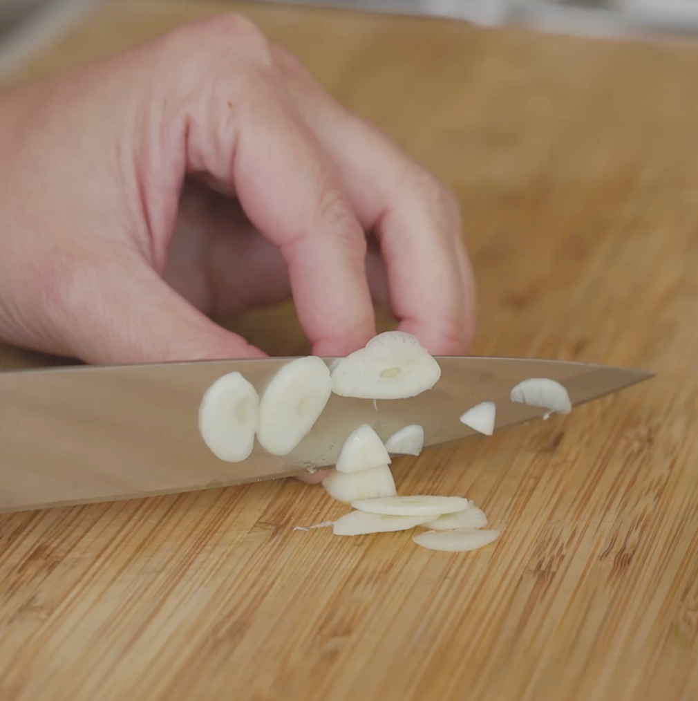 slicing garlic on a cutting board with a knife