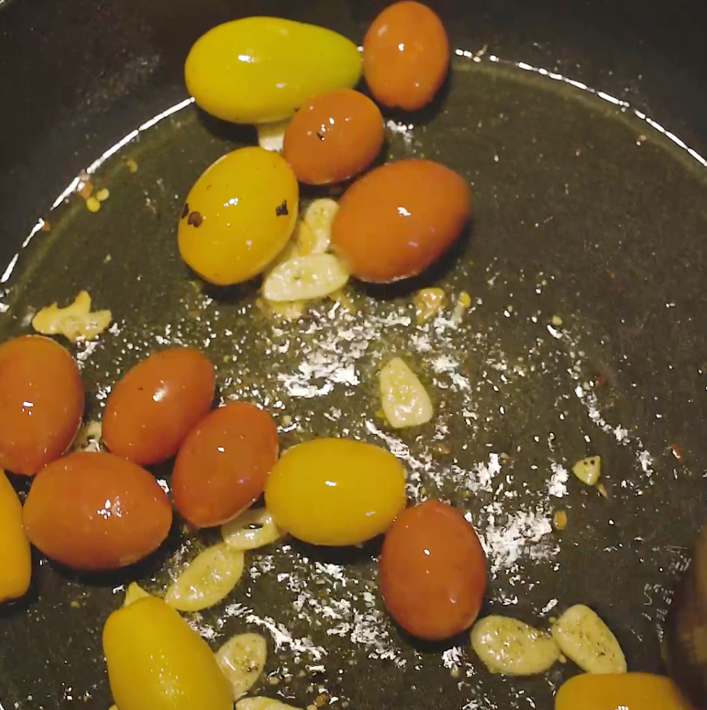 cherry tomatoes  and garlic cloves cooking in a pan