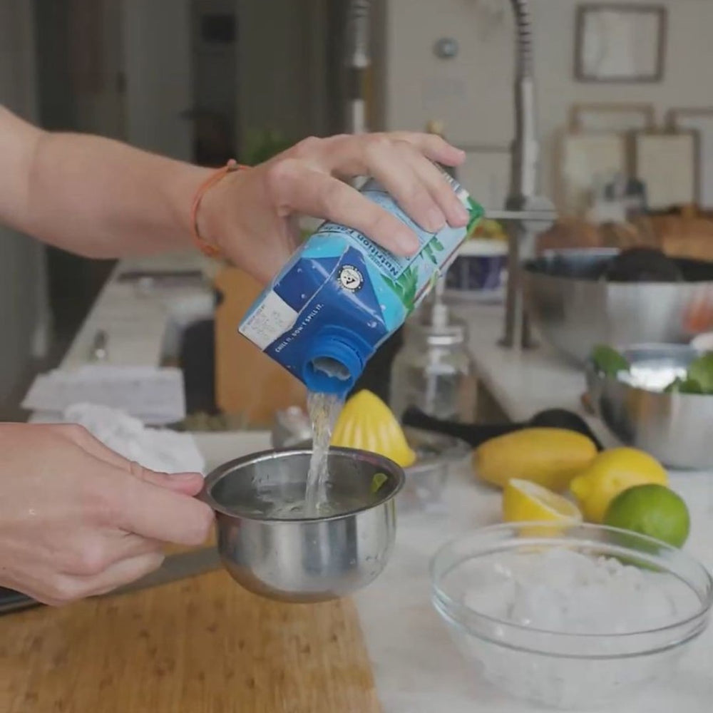 pouring coco water into a measuring cup in a kitchen setting