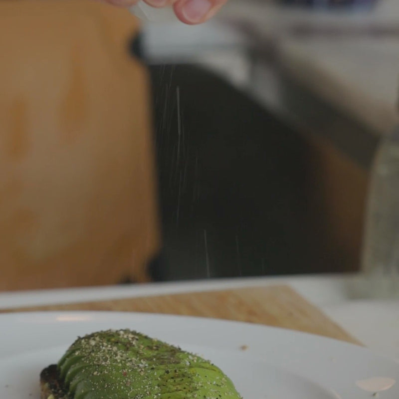 sprinkling seasoning over avocado toast