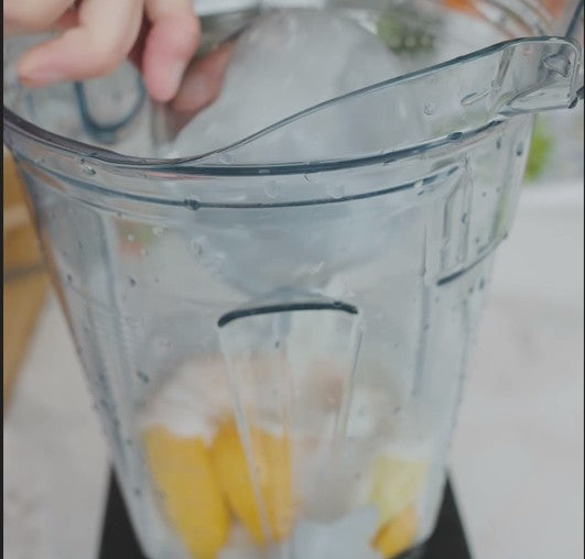 adding ice to a blender with mango slices